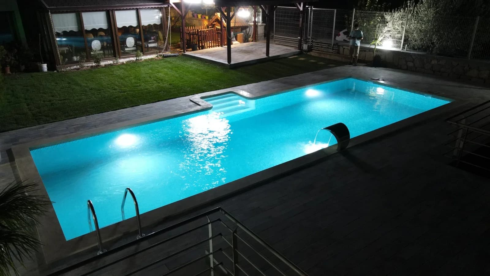 Gece aydınlatmalı bahçe havuzu, paslanmaz su perdesi ve ahşap deck