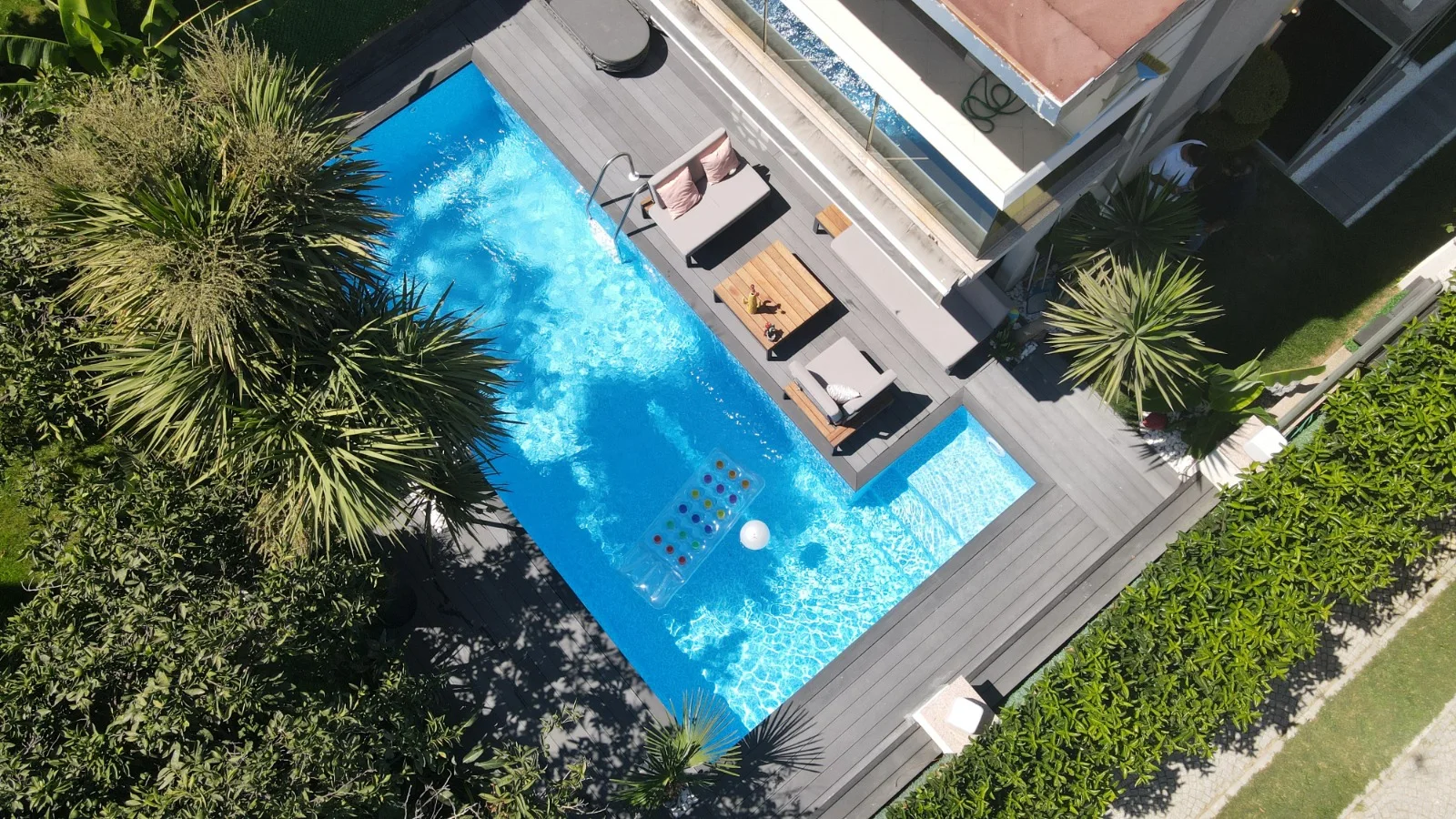 Villa bahçesinde deck, oturma grubu ve sığ çocuk bölgesiyle birlikte planlanmış prefabrik havuz — kuş bakışı görünüm