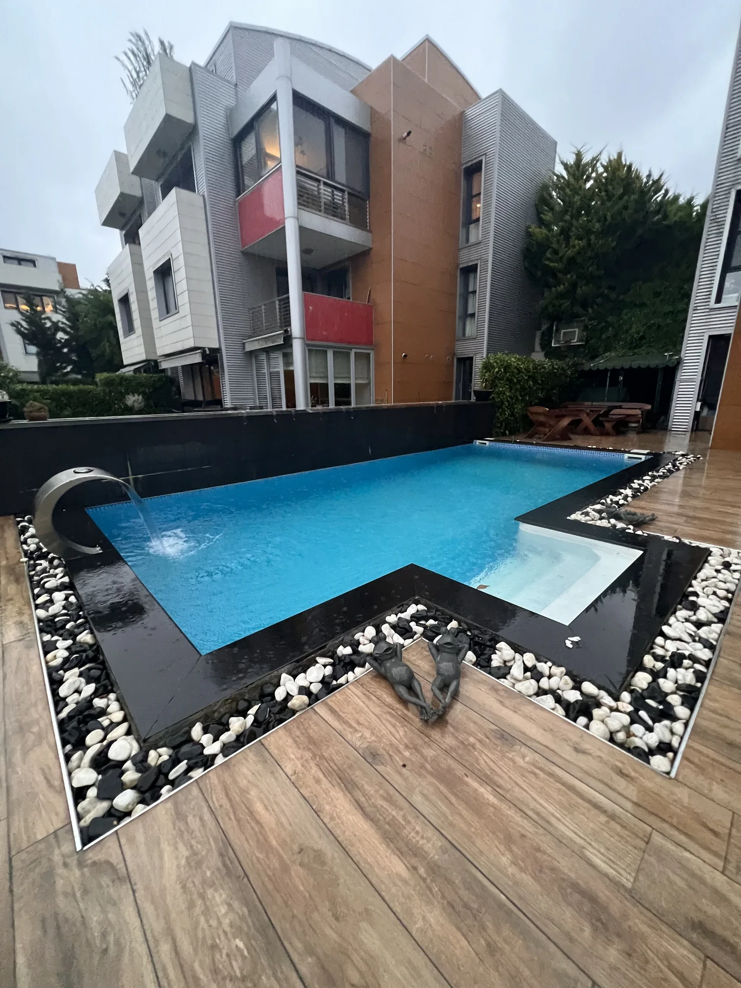 Villa bahçesinde L formlu Fiplus havuz, granit kenar ve ahşap görünümlü zemin kaplamasıyla — ölçü ve form maliyeti belirleyen ilk kalemdir